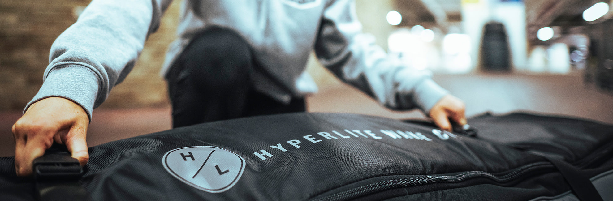 Person zipping a large black Hyperlite Mountain Gear bag in an indoor setting.