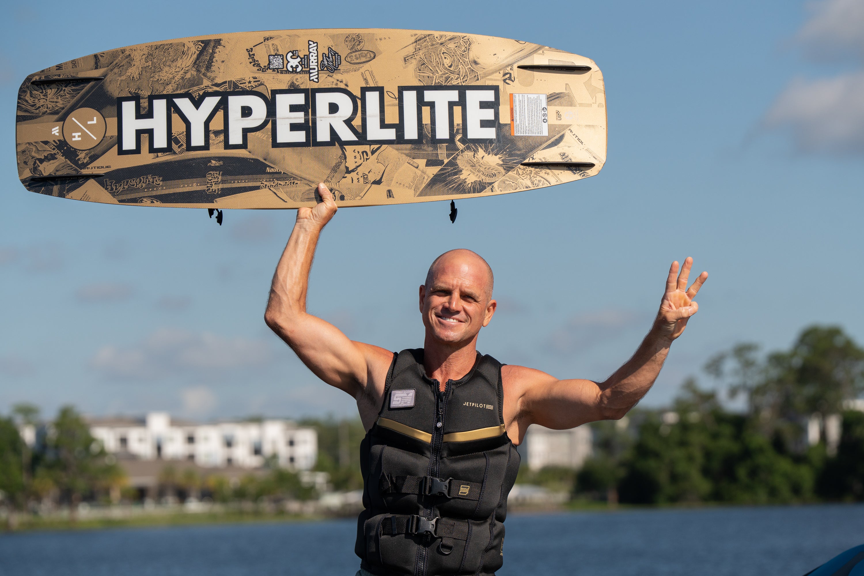 Person smiling and holding Murray Pro board overhead while standing near the water.