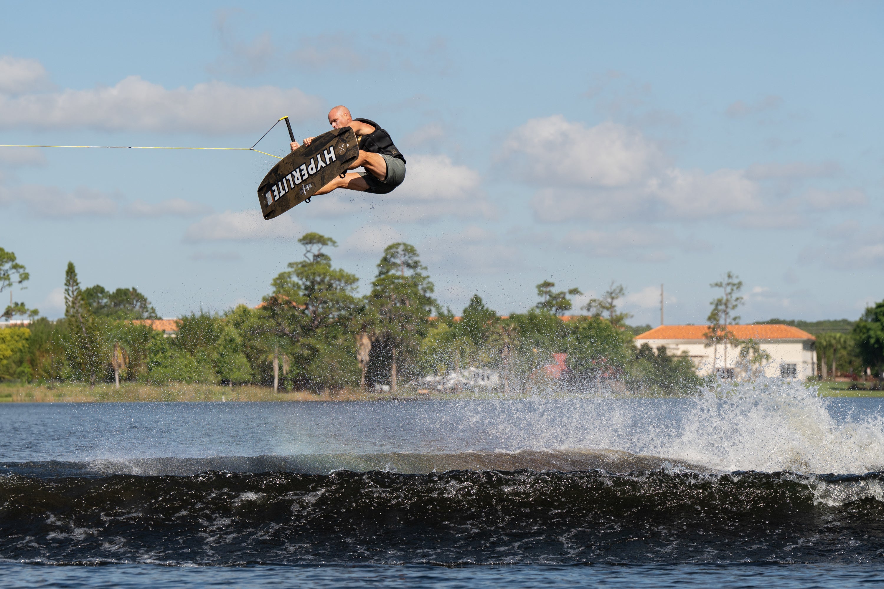 Wakeboarder airborne above the lake, performing a trick with knees bent and handle in hand.