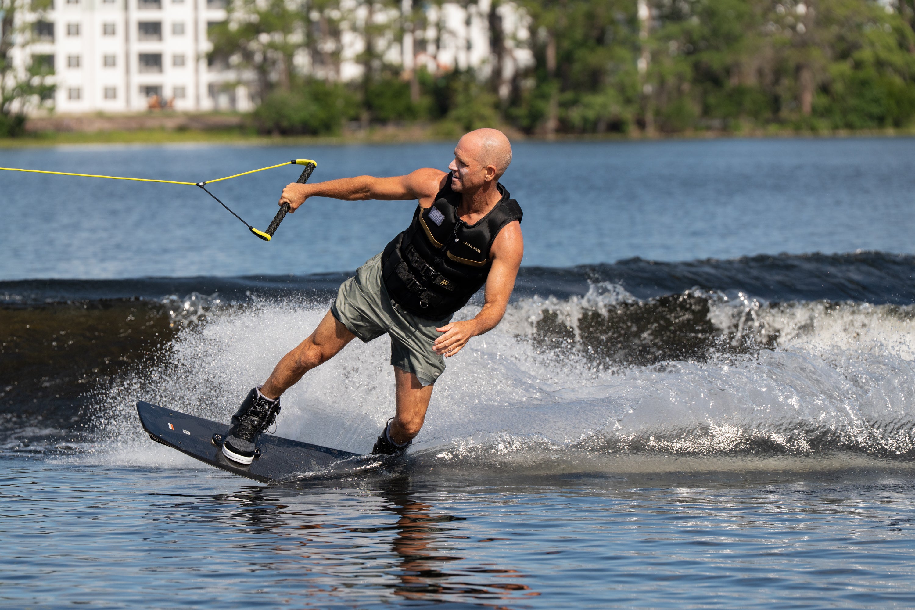 Wakeboarder in motion carving across the water, holding a yellow rope and leaning into the turn.