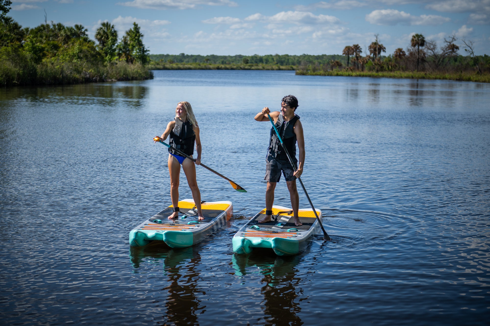 Two people paddleboarding on a calm lake under a partly cloudy sky.