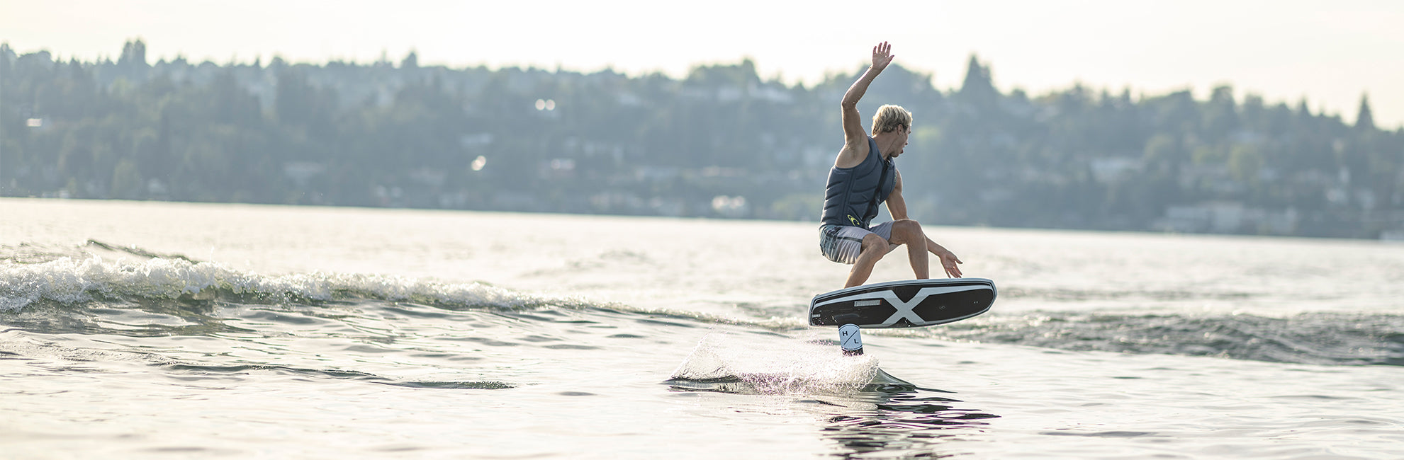 Person wakeboarding on a lake, performing a jump with a cityscape in the hazy background.