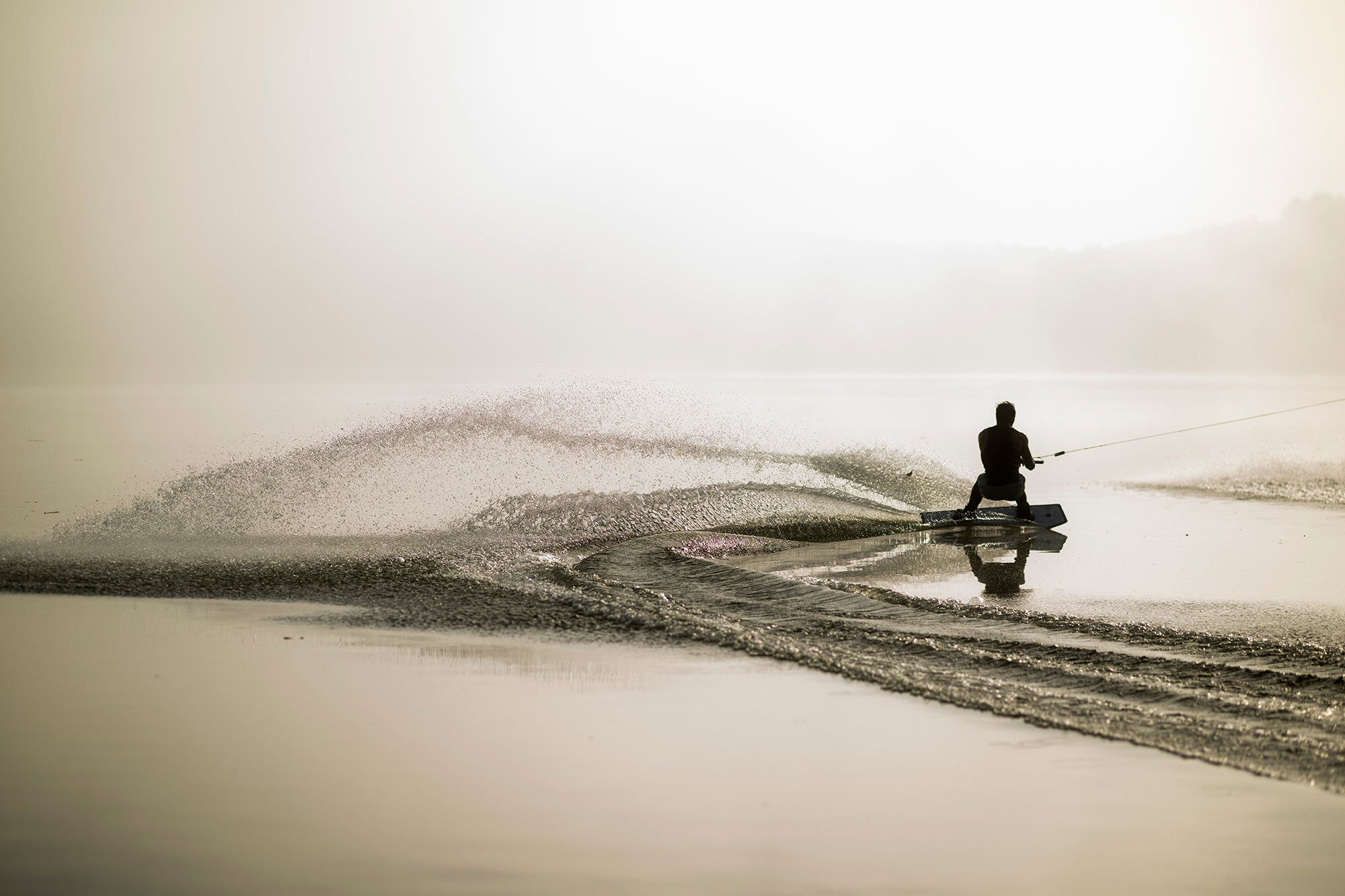 Silhouette of a person waterskiing on a calm lake, with a splash trailing behind them in the serene setting.