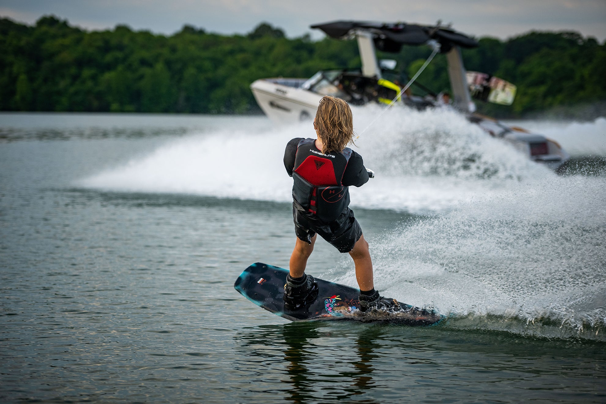 Person wakeboarding on a lake with a speedboat creating waves in the background.