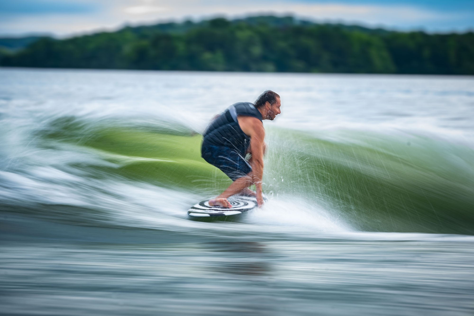 Man surfing a wave on a body of water with trees in the background.