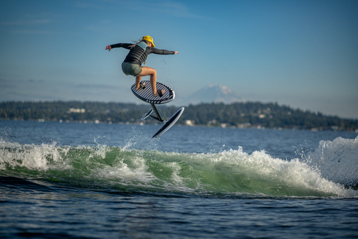 A person wearing a helmet is riding a hydrofoil board over a wave on a sunny day.