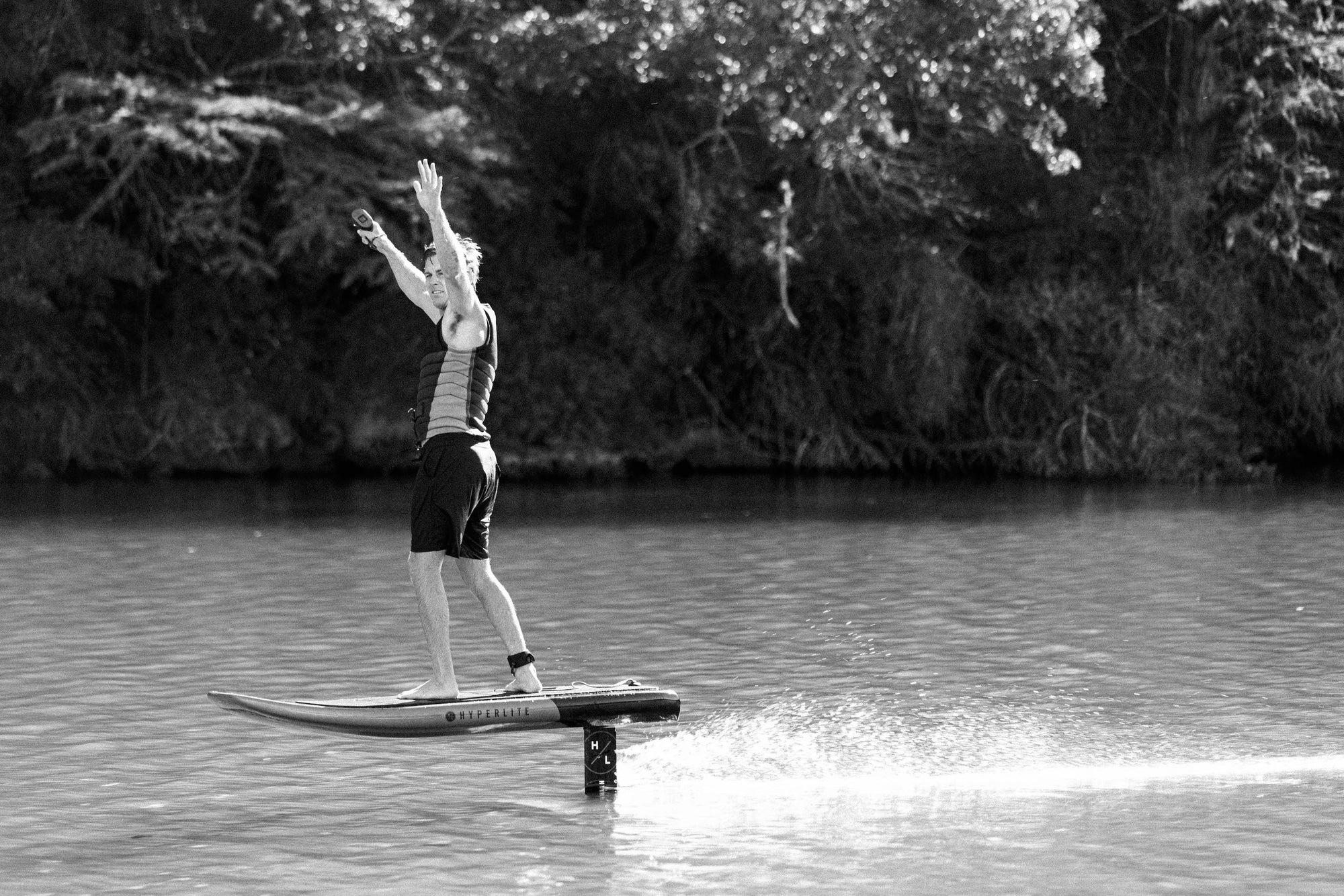 Rider standing on the Stratos e-foil board above the water with arms raised, black and white image.