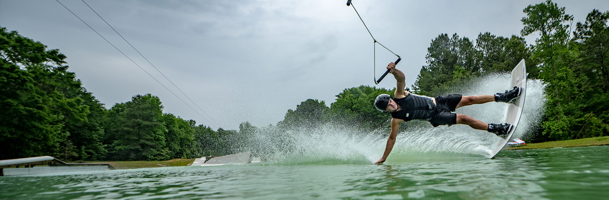 Person wakeboarding on a lake, creating a splash with trees in the background.