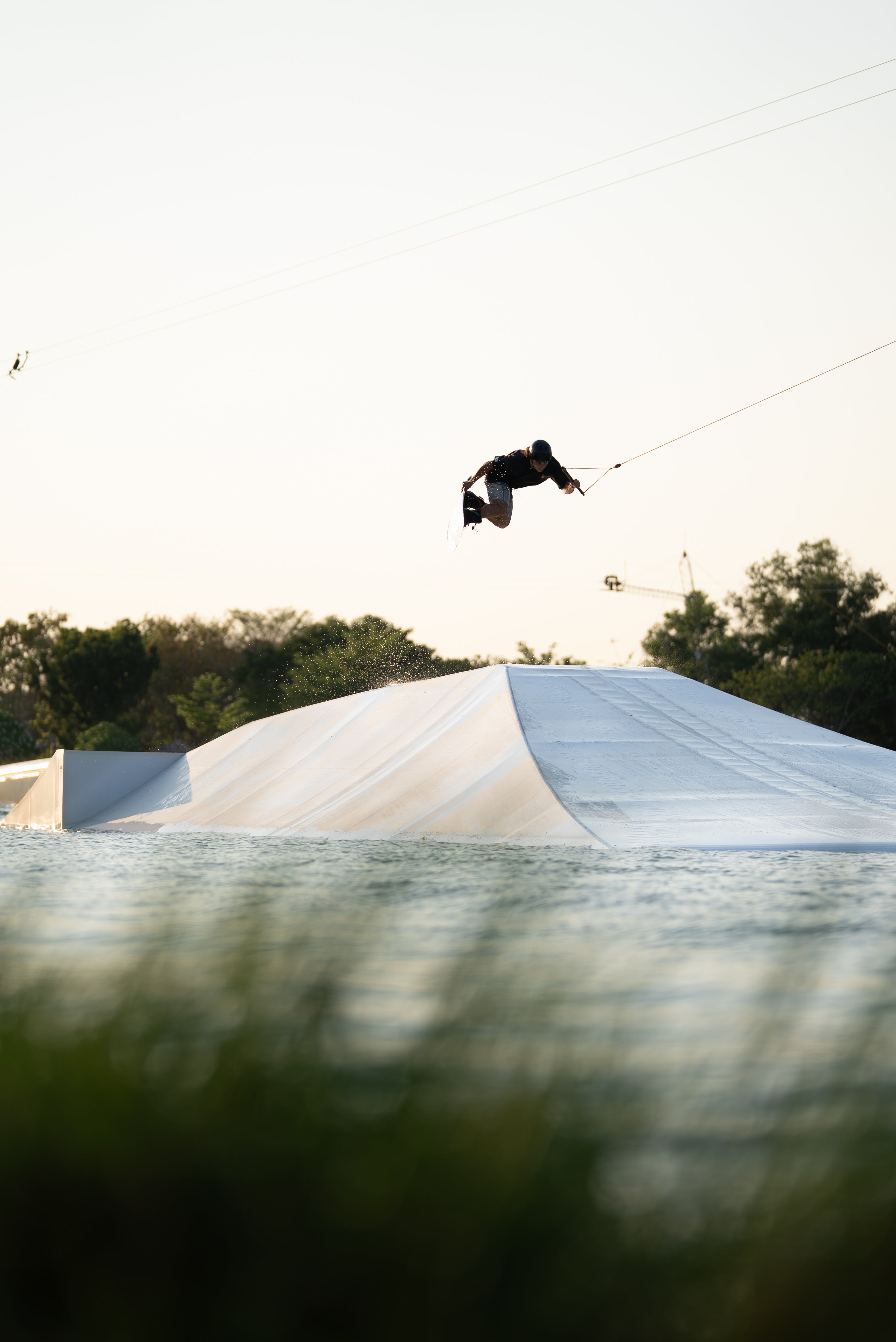 Person wakeboarding and jumping off ramp on a sunny day.