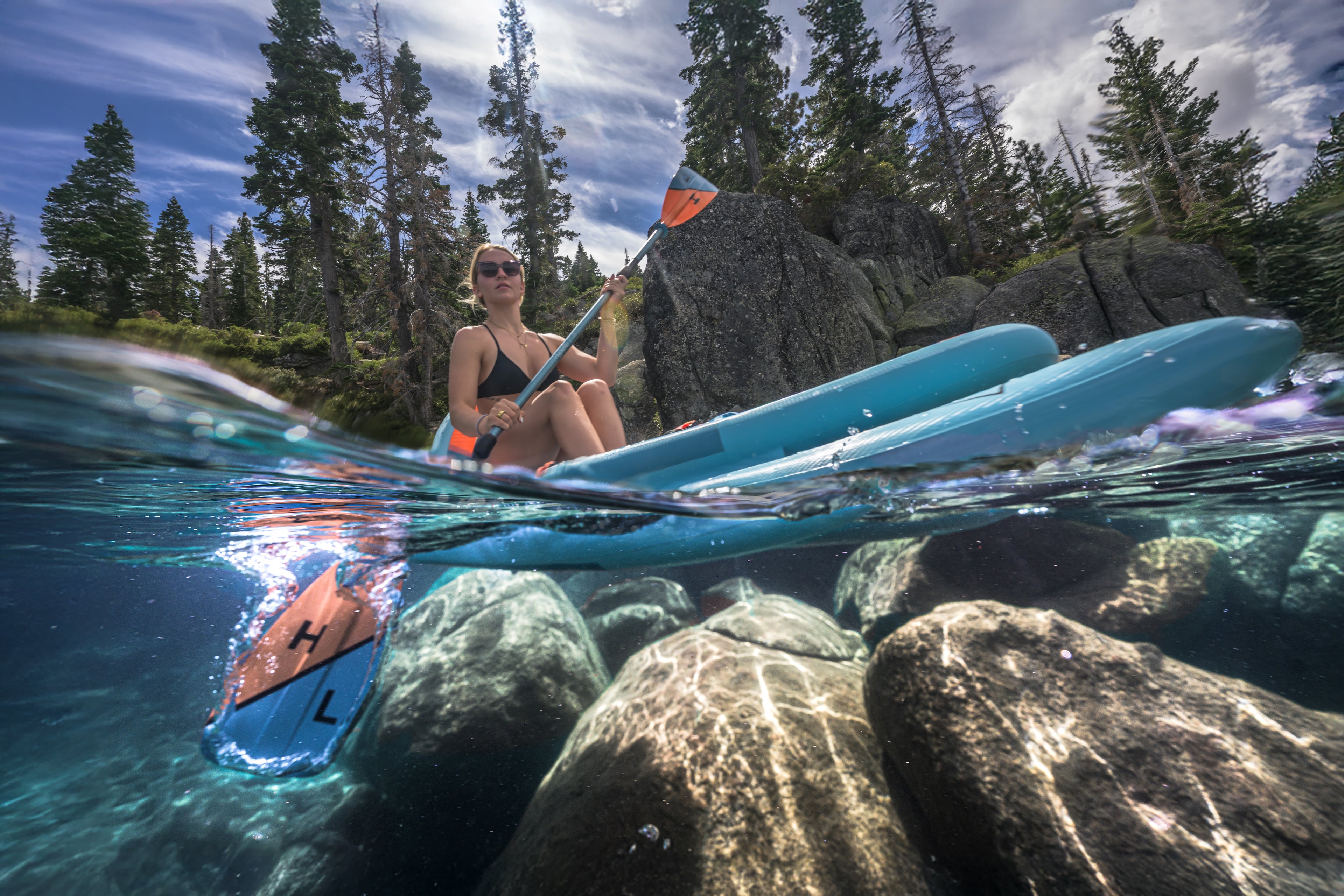 Woman kayaking in a forested lake with clear water and rocks.