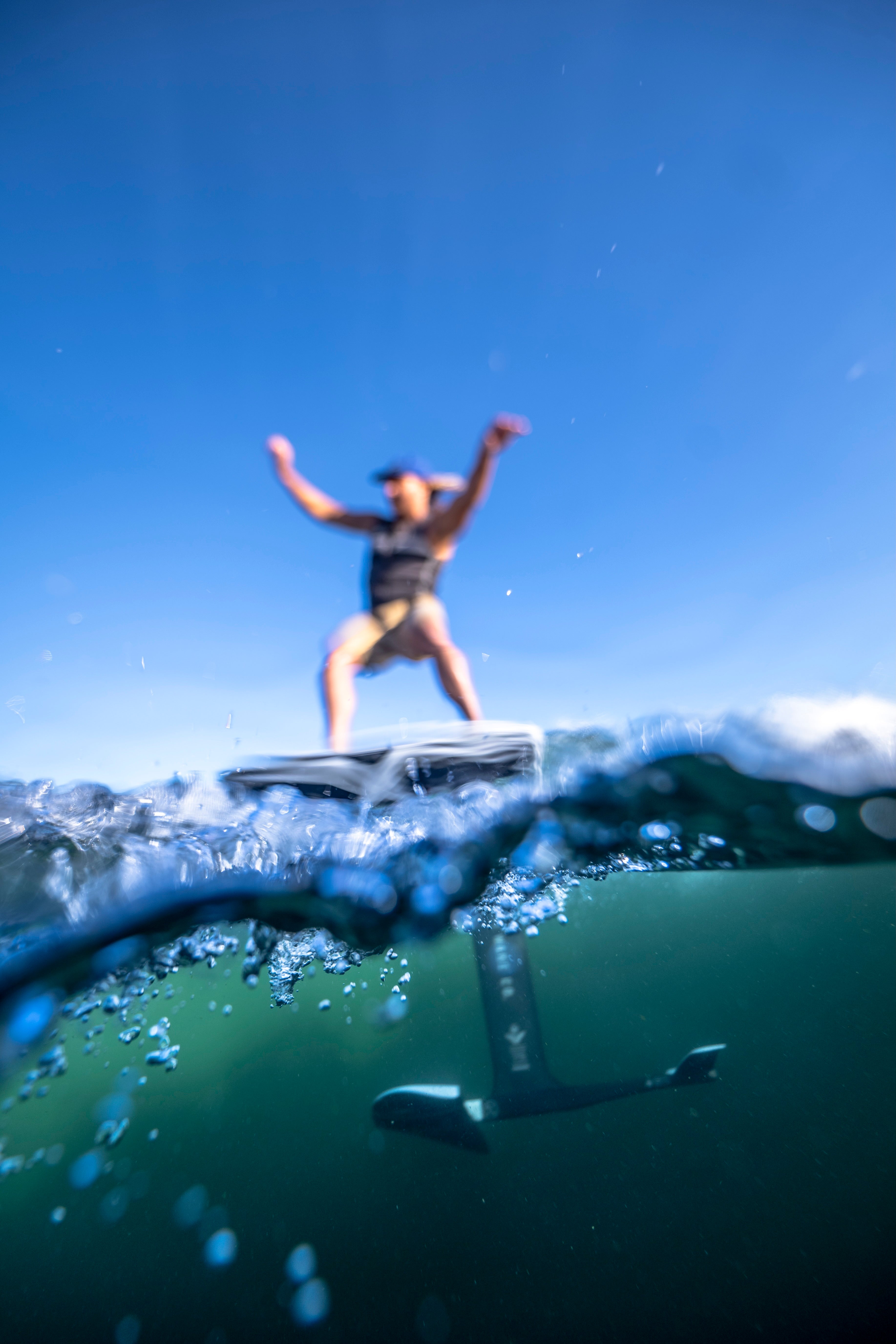 Person surfing on a foil board above ocean waves under a clear blue sky.