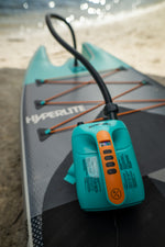 Close-up of an electric pump inflating an Elevation II - iSUP Paddle Board on a sandy beach.