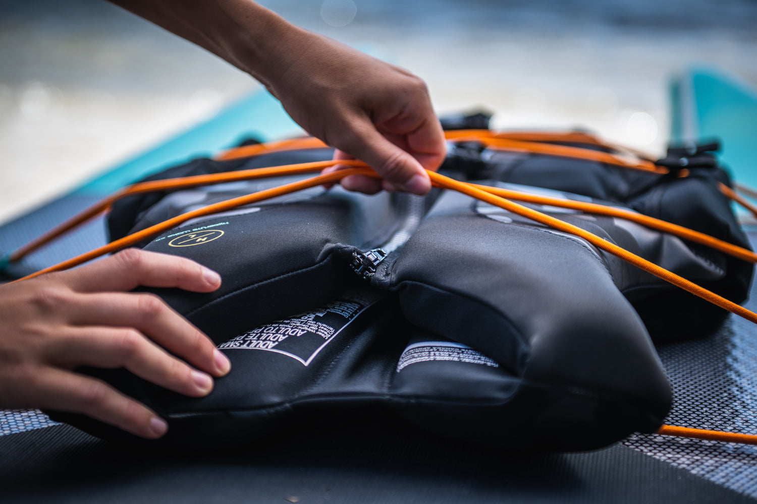 Hands securing a black life vest with orange cords on the Elevation II - iSUP Paddle Board.