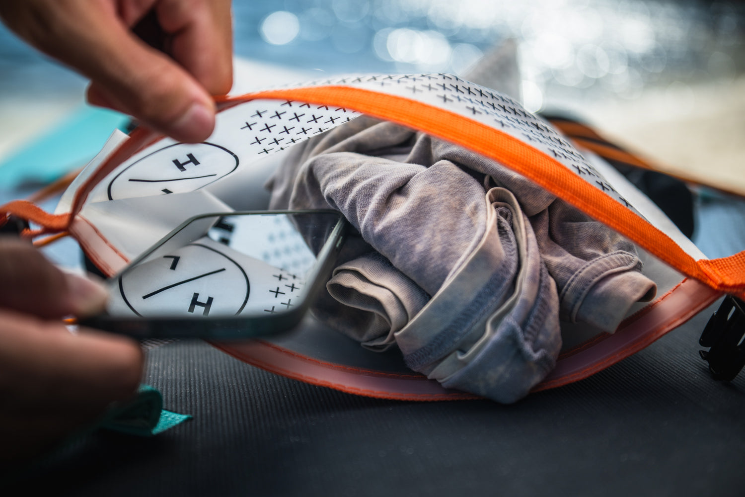 Hands holding an open bag with clothes and the Elevation II - iSUP Paddle Board.