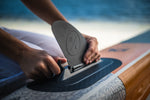 Person attaching an Elevation II fin with Nano-Fuse tech to a paddleboard by the water.