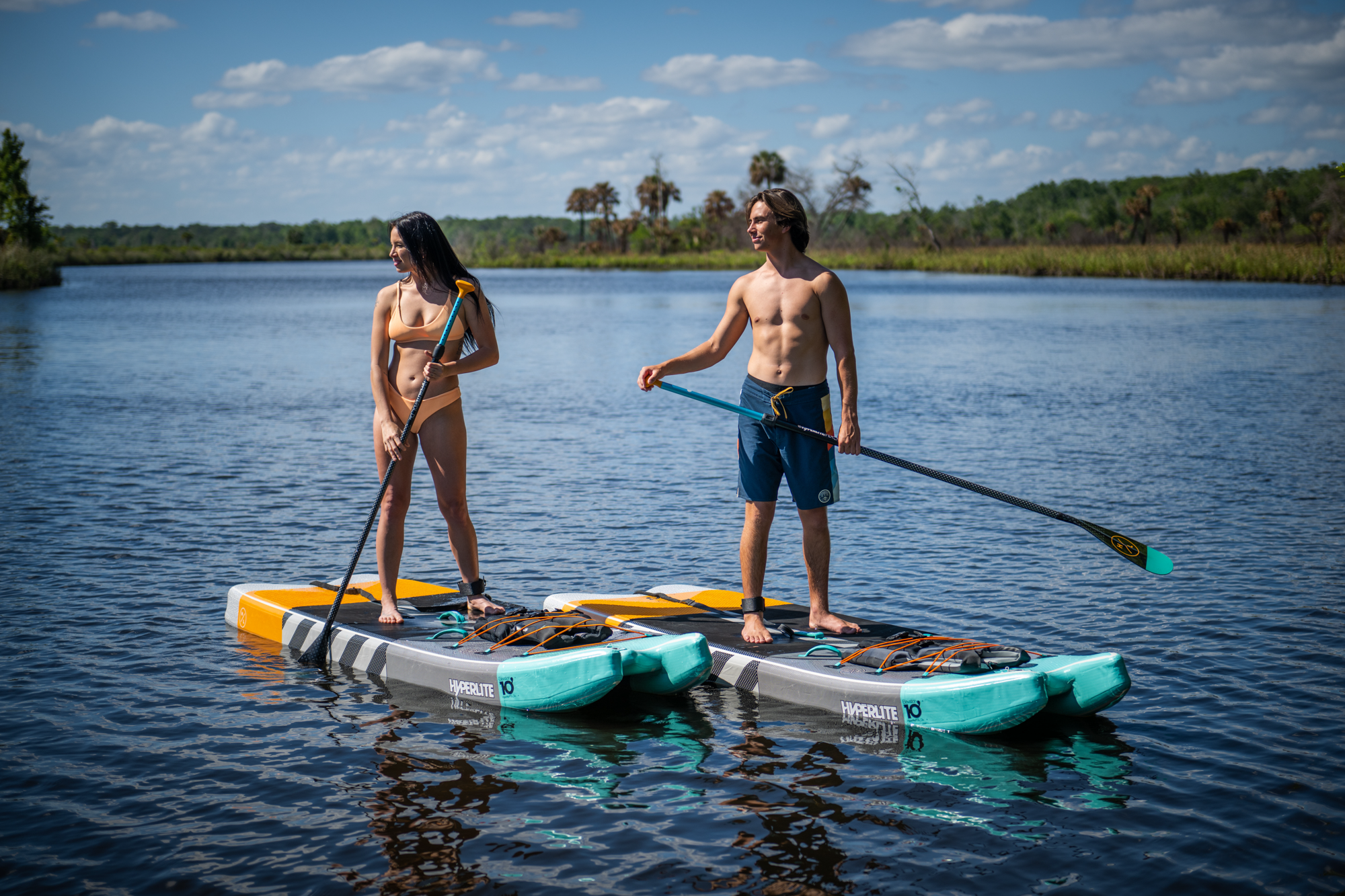 Two people on paddleboards on a calm lake with trees in the background.