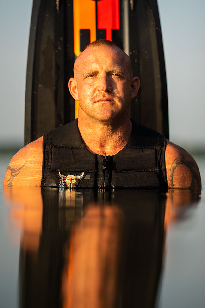 Man in a black life vest partially submerged in water, with skis visible behind him.