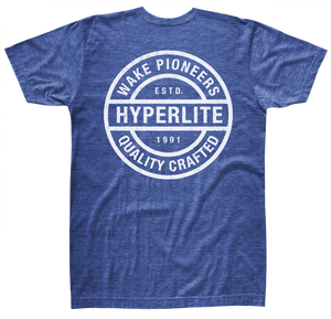 Back view of a royal blue short-sleeve t-shirt with a large white circular graphic that reads ‘Wake Pioneers, Hyperlite, Quality Crafted, Estd. 1991.