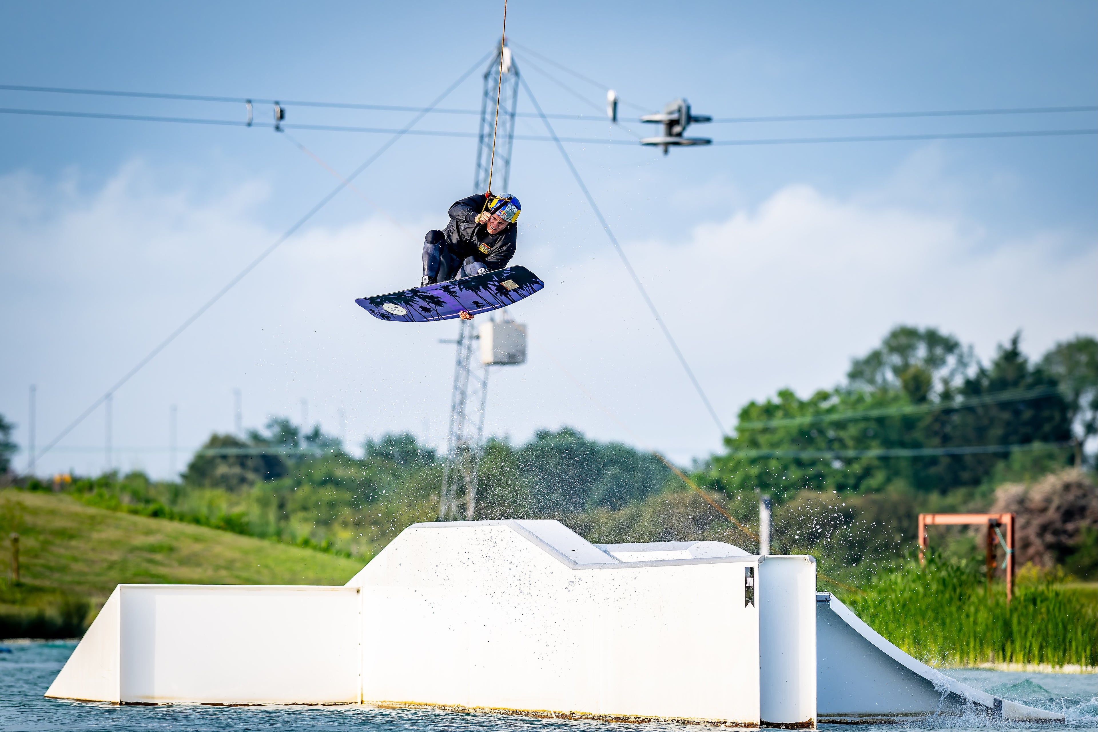 Person wakeboarding in mid-air with a cable and ramp in the background.