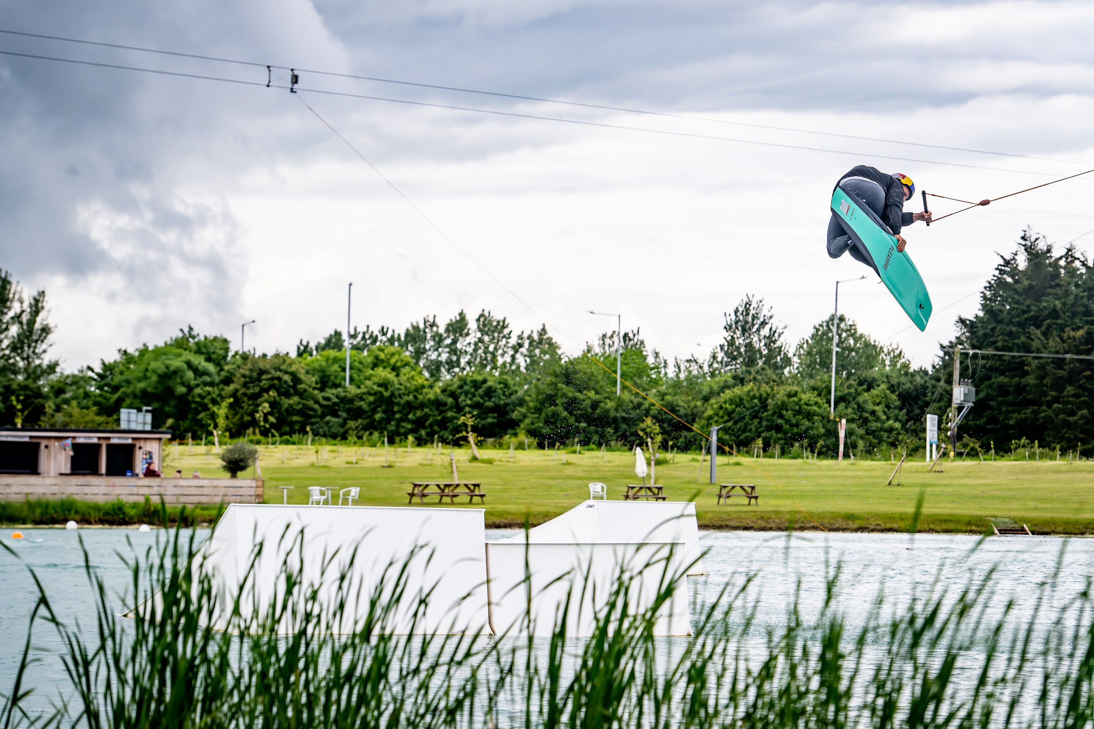 Person wakeboarding and performing a high jump at a cable park.