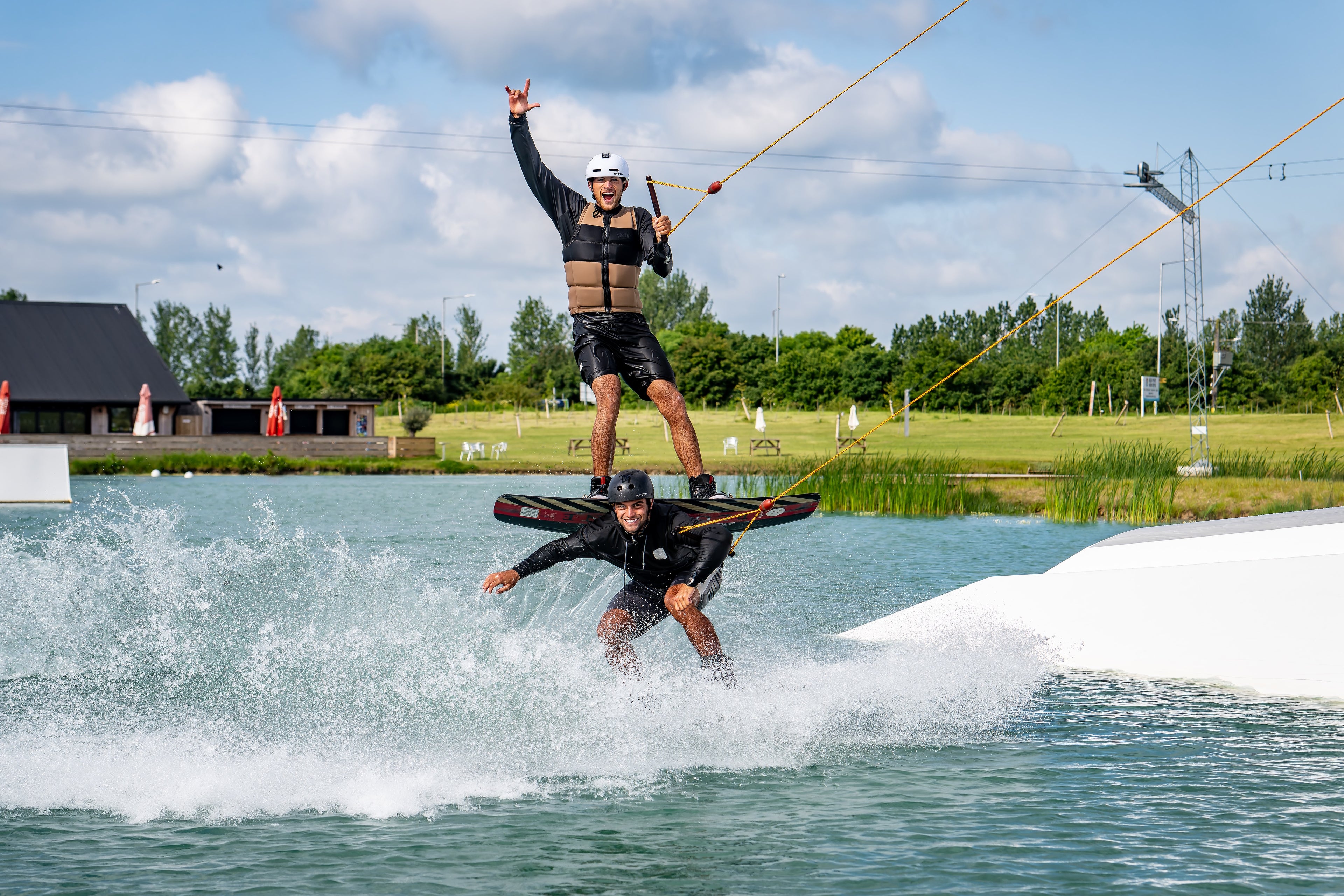 Two people wakeboarding on a lake; one stands on the others shoulders.