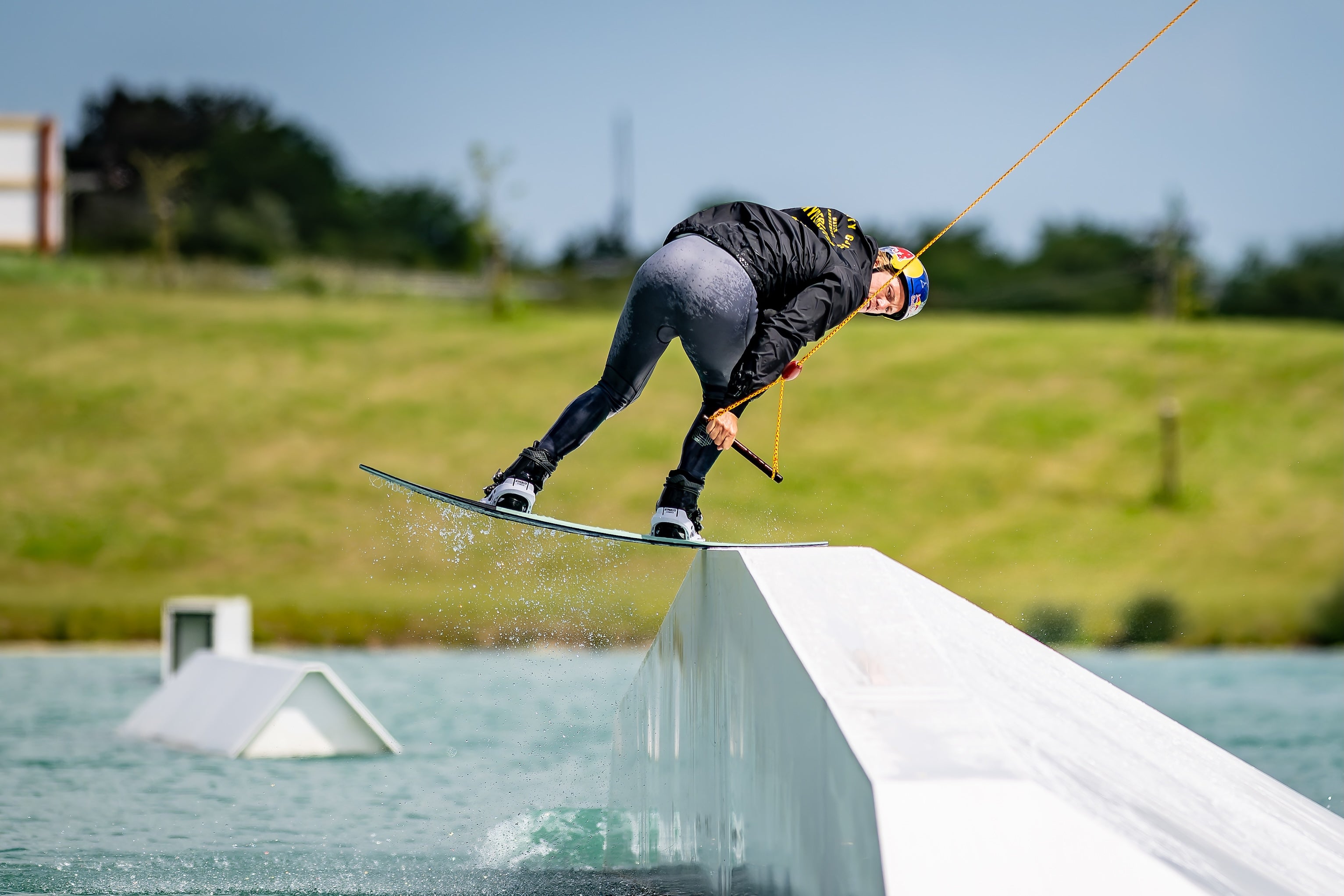 Person wakeboarding on a rail with green field in background.
