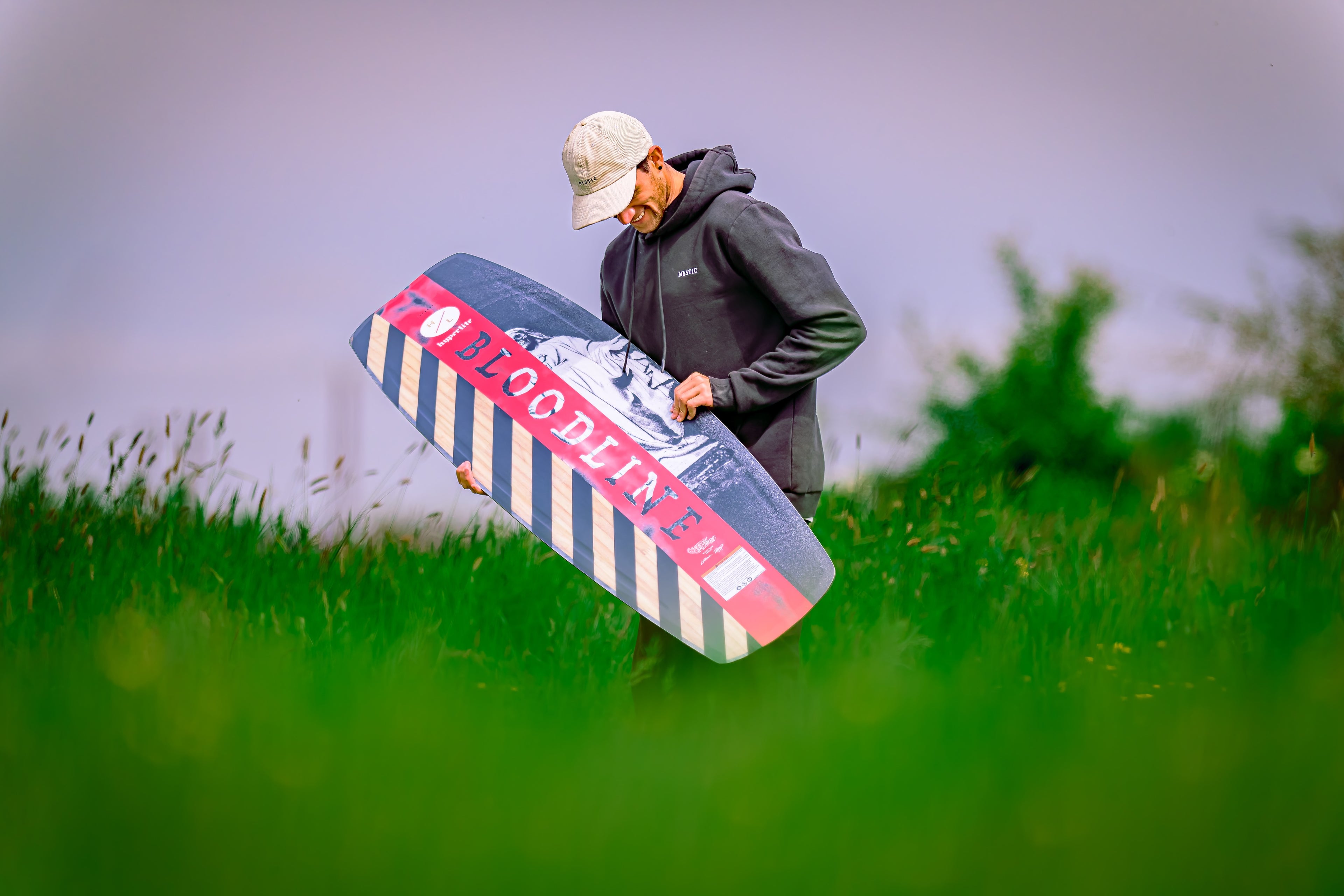 Person in a hoodie carrying a board in a grassy field.