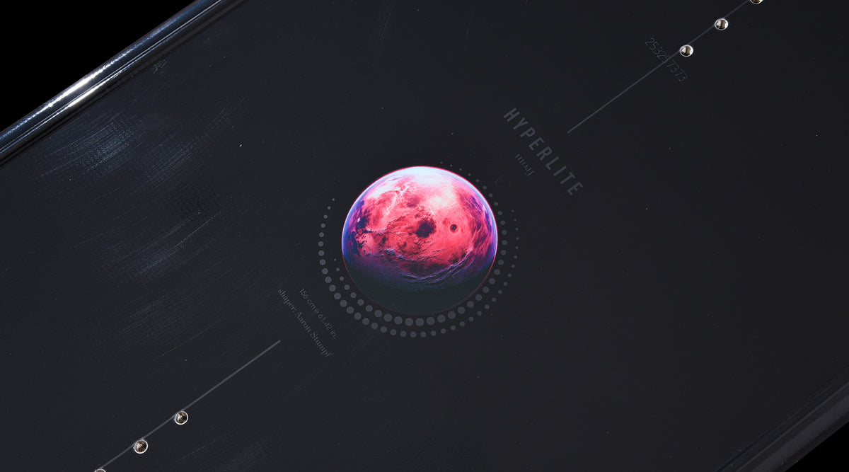 Close-up of pink planet graphic detail on the black deck of the Pleasure wakeboard.