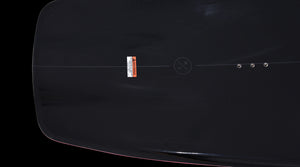 Close-up of mounting inserts and warning label on the black deck of the Pleasure wakeboard.