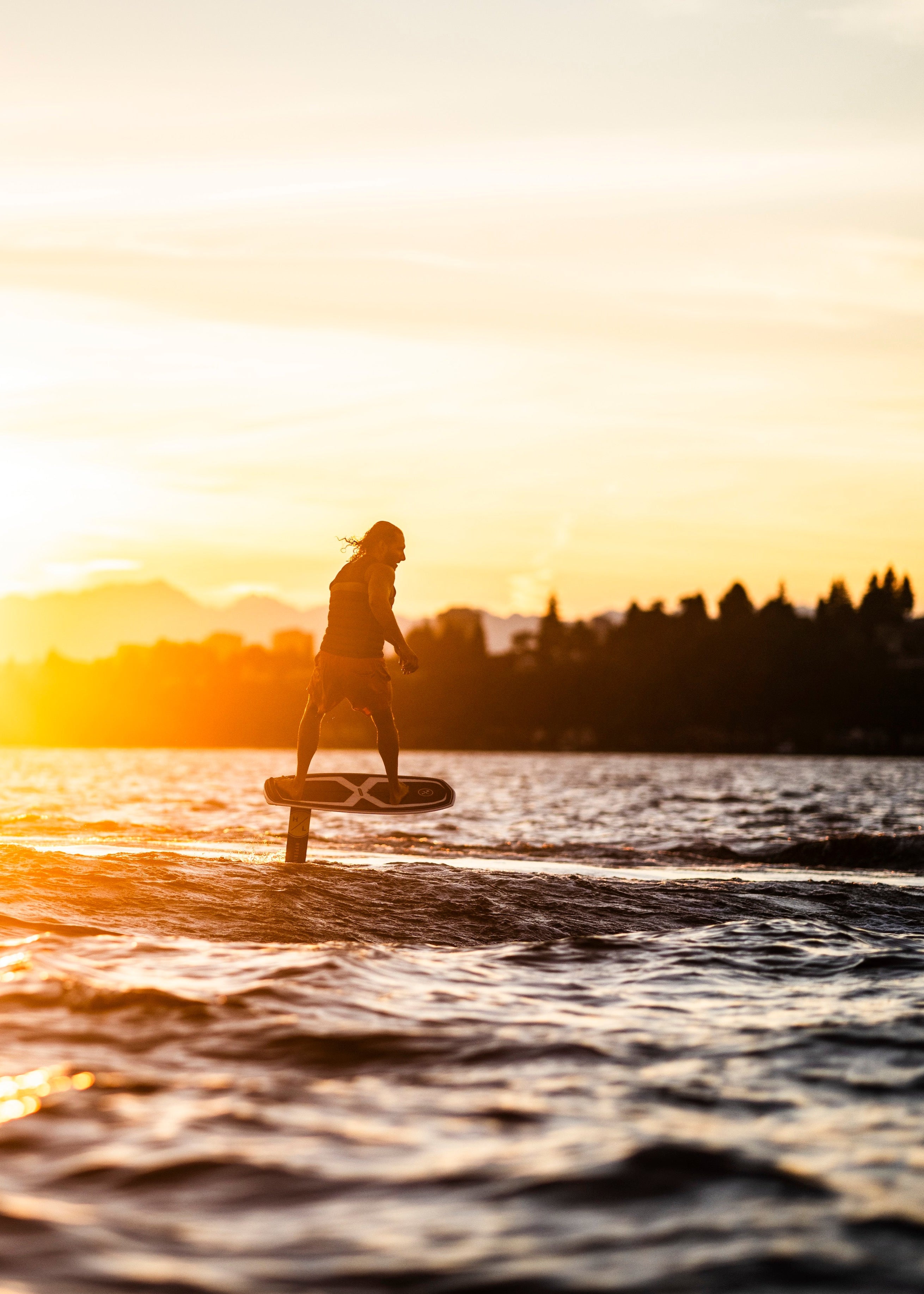 Person foil surfing on water at sunset with distant mountains in view.