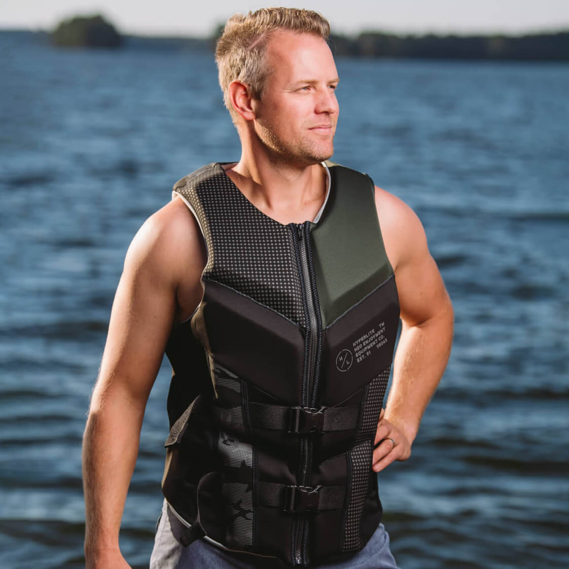 Person wearing a sleeveless life vest standing near a lake.
