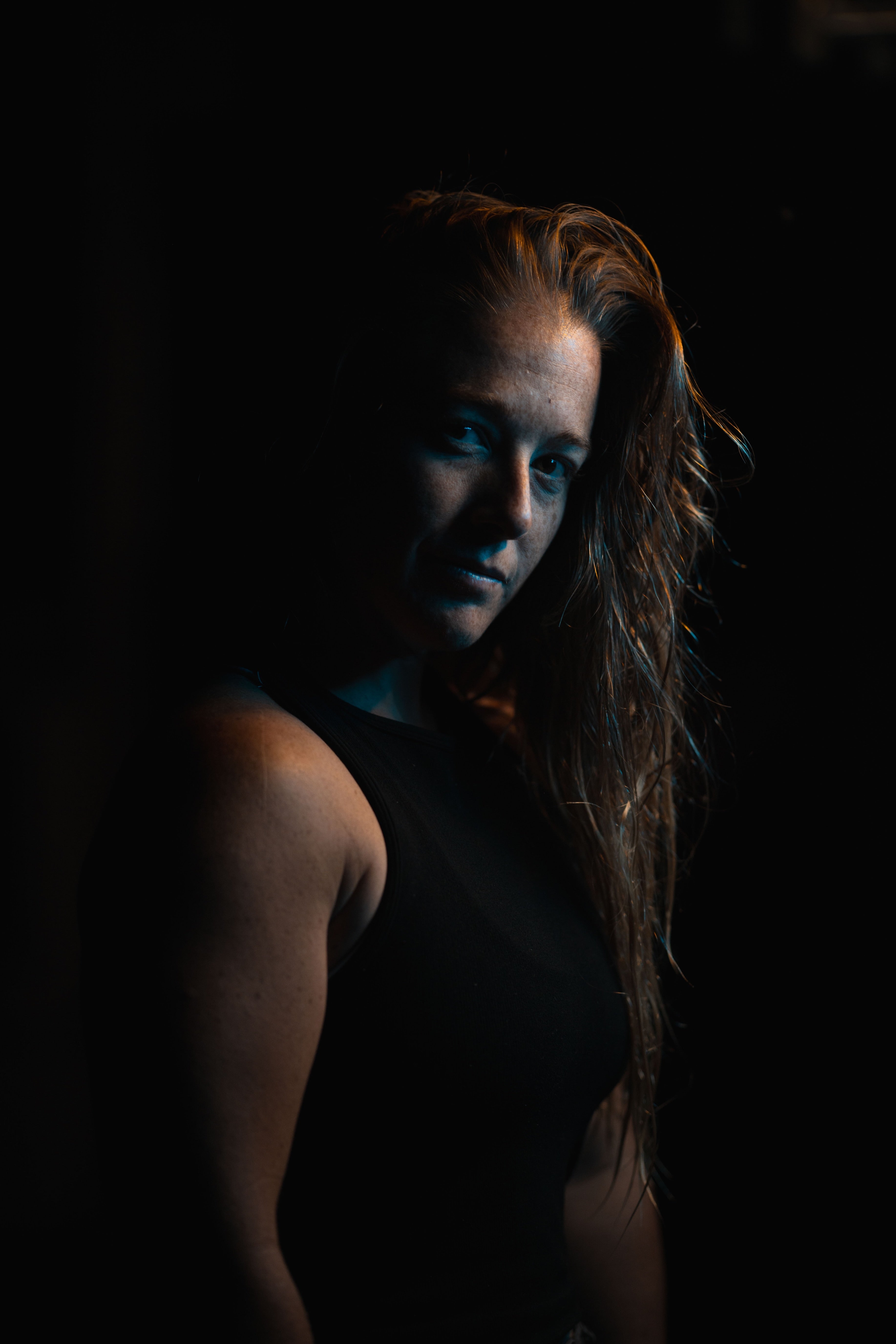 Person with wet hair in dark lighting, wearing a sleeveless top, looking towards the camera.
