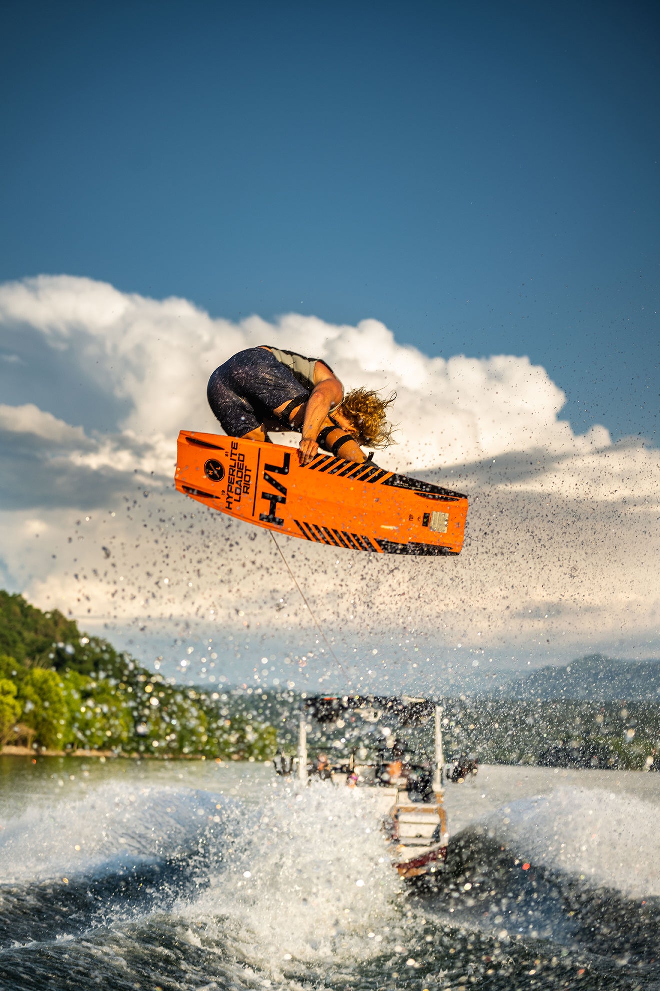 Person wakeboarding, performing an airborne trick with a vibrant orange board over the water.