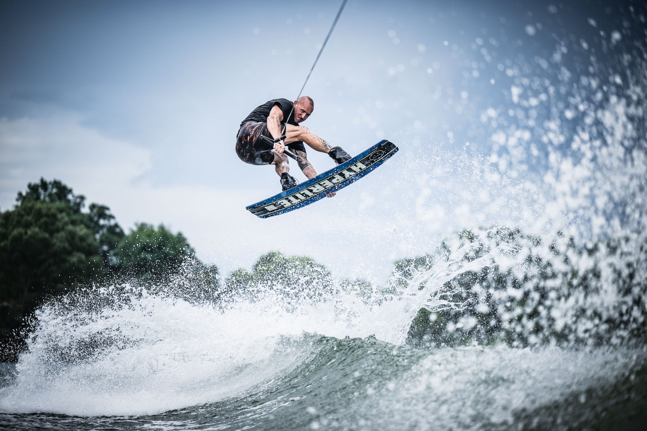 Person wakeboarding on a wave with a clear sky and trees in the background.