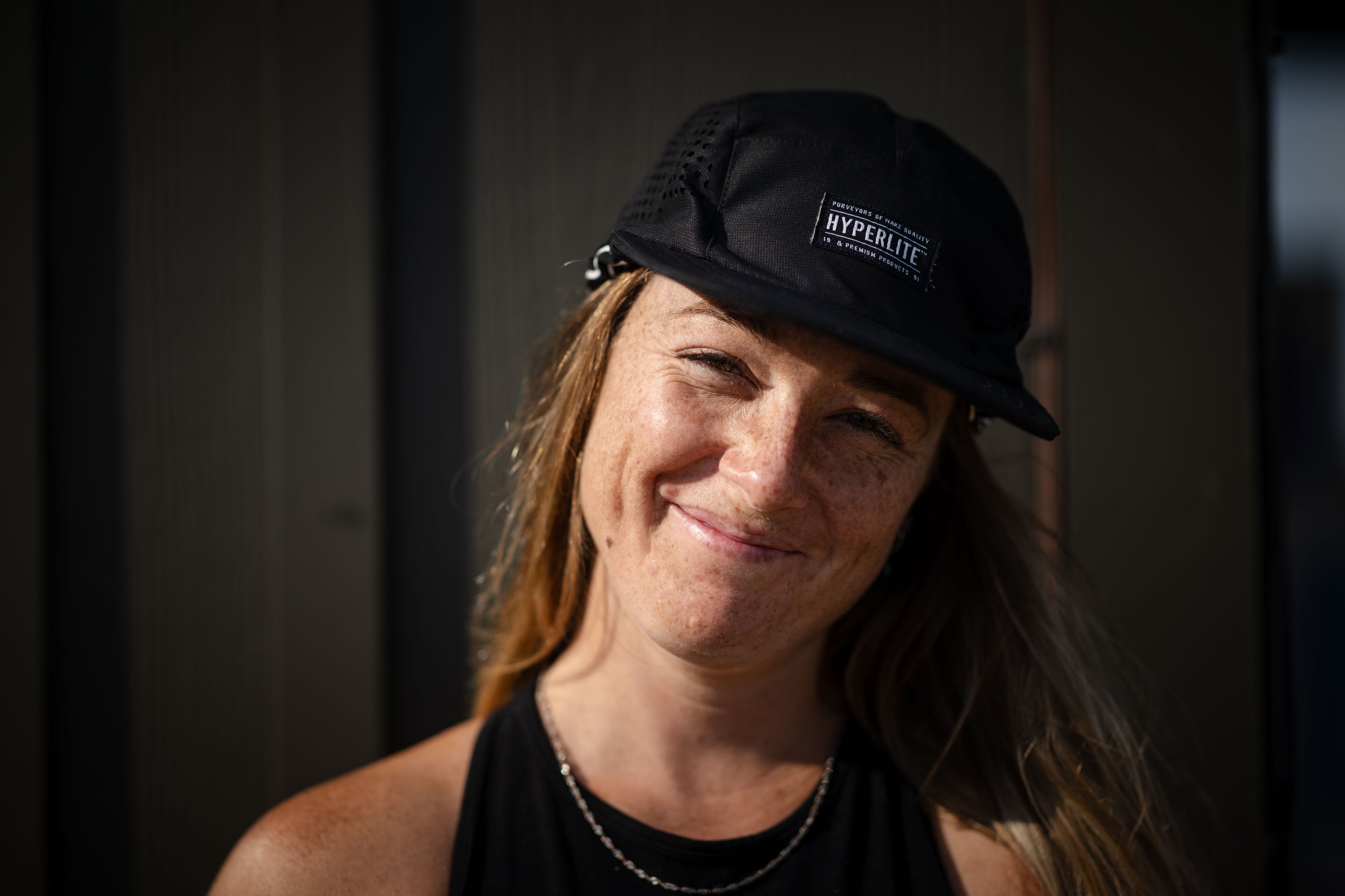 Smiling person wearing a black hat and shirt against a dark background.