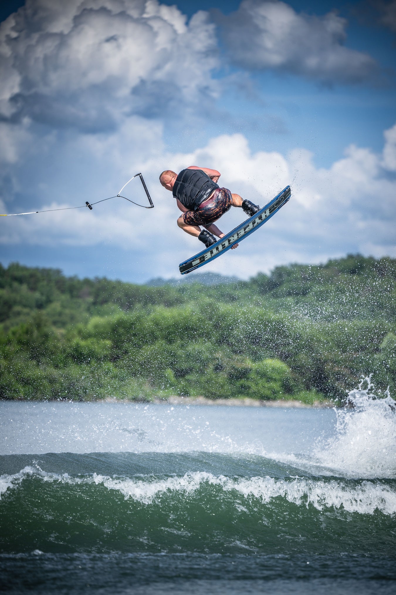 Person wakeboarding on a lake with trees and clouds in the background.