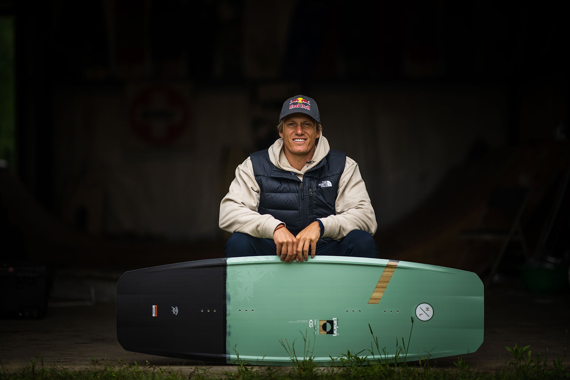 Person sitting indoors, smiling, holding a wakeboard vertically in front of them.