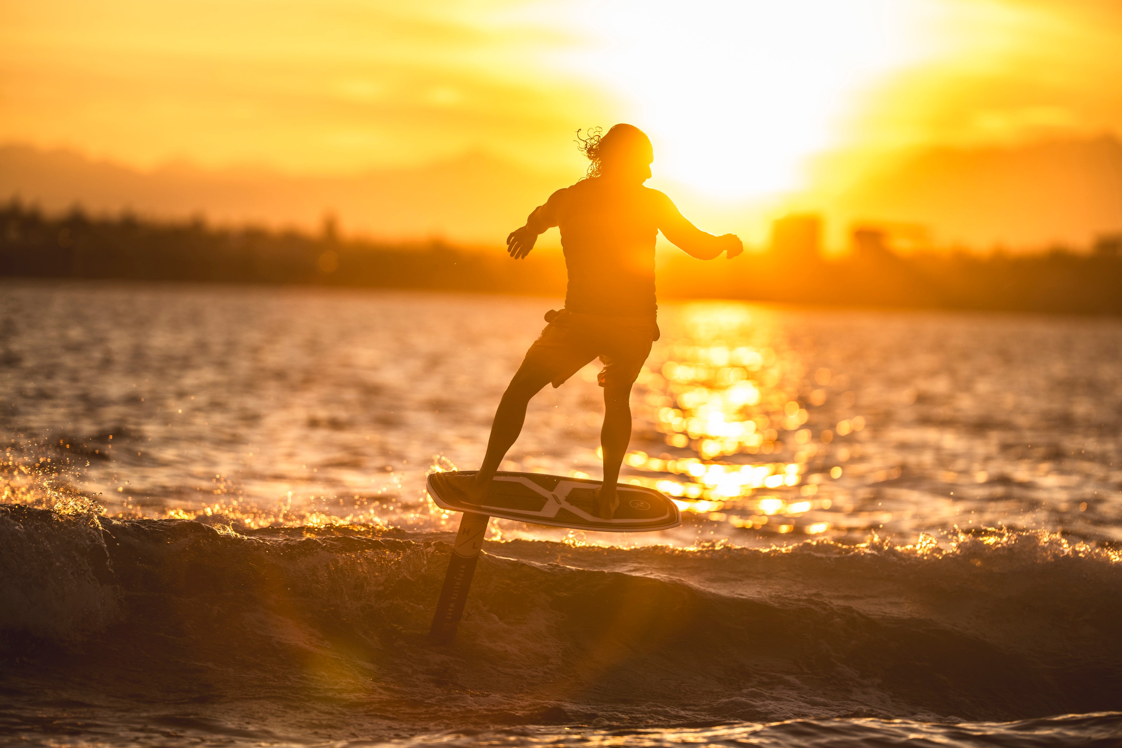 Silhouette of a person surfing at sunset on a foil board.