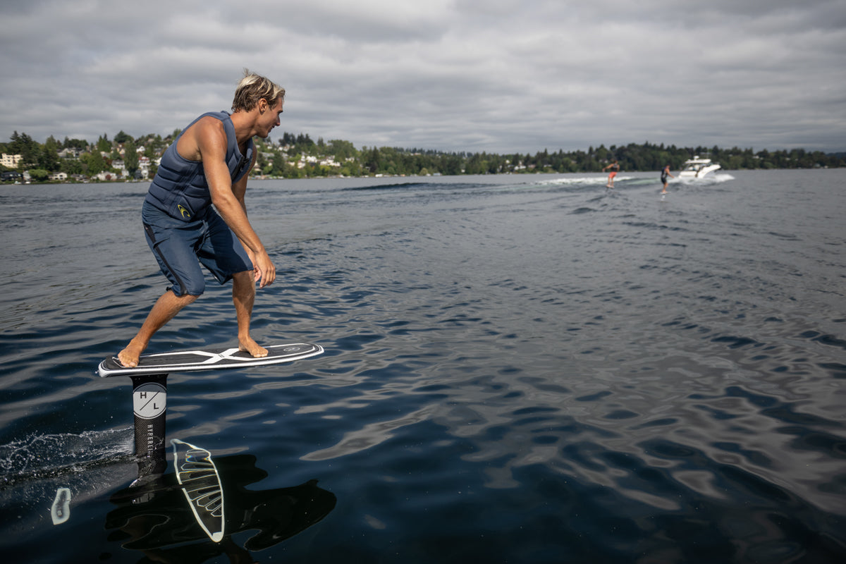Person hydrofoiling on a lake with Starship w/Raptor 1100 Foil Kit, boats, and trees nearby.