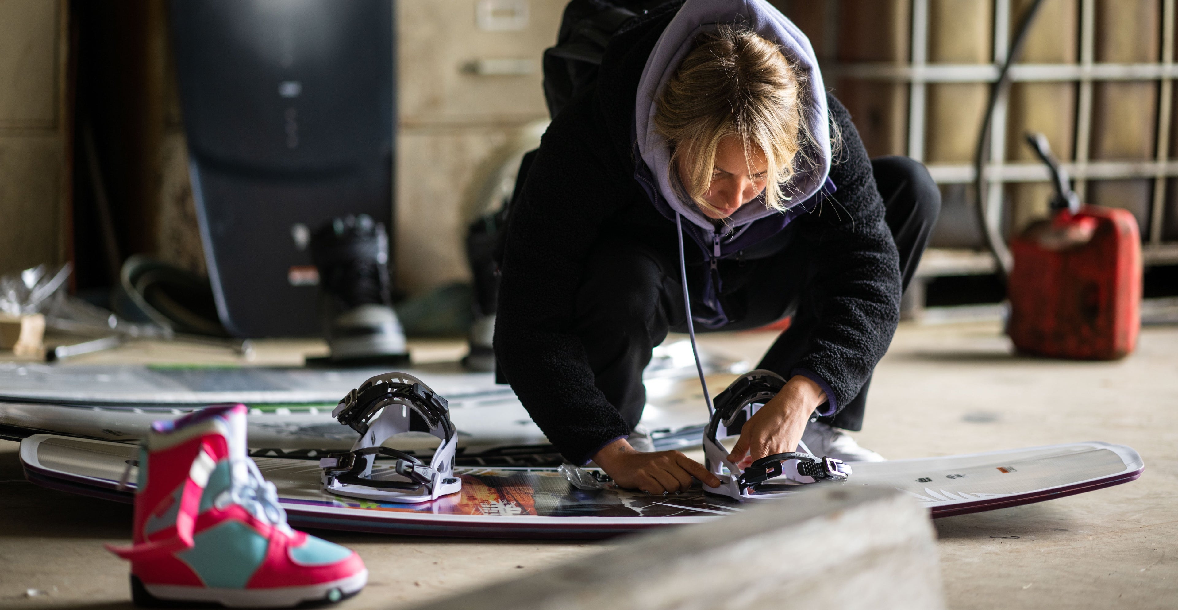 Person adjusting bindings on a snowboard inside a workshop.