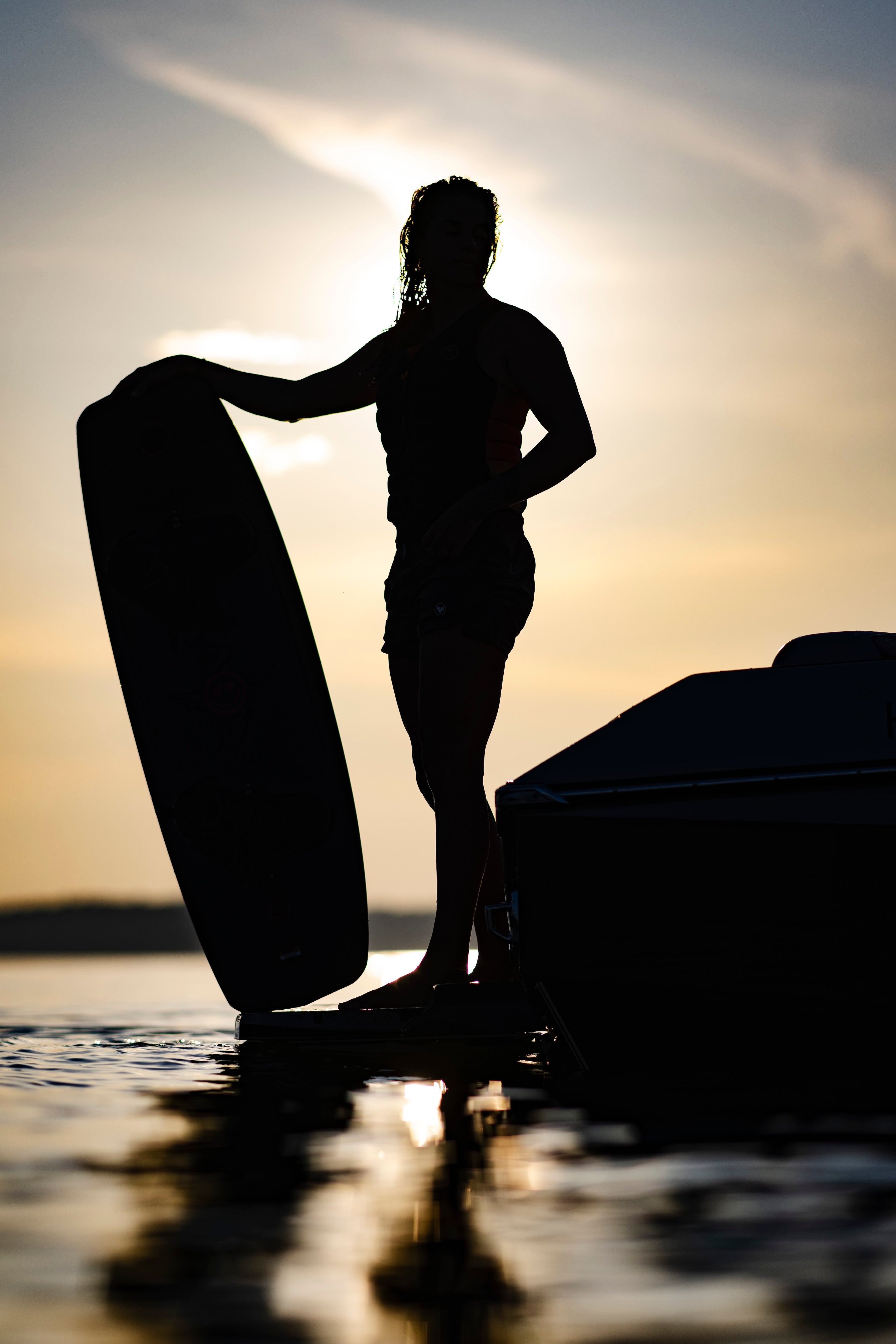 Silhouette of a person and wakeboard against a sunset on the water with a boat.