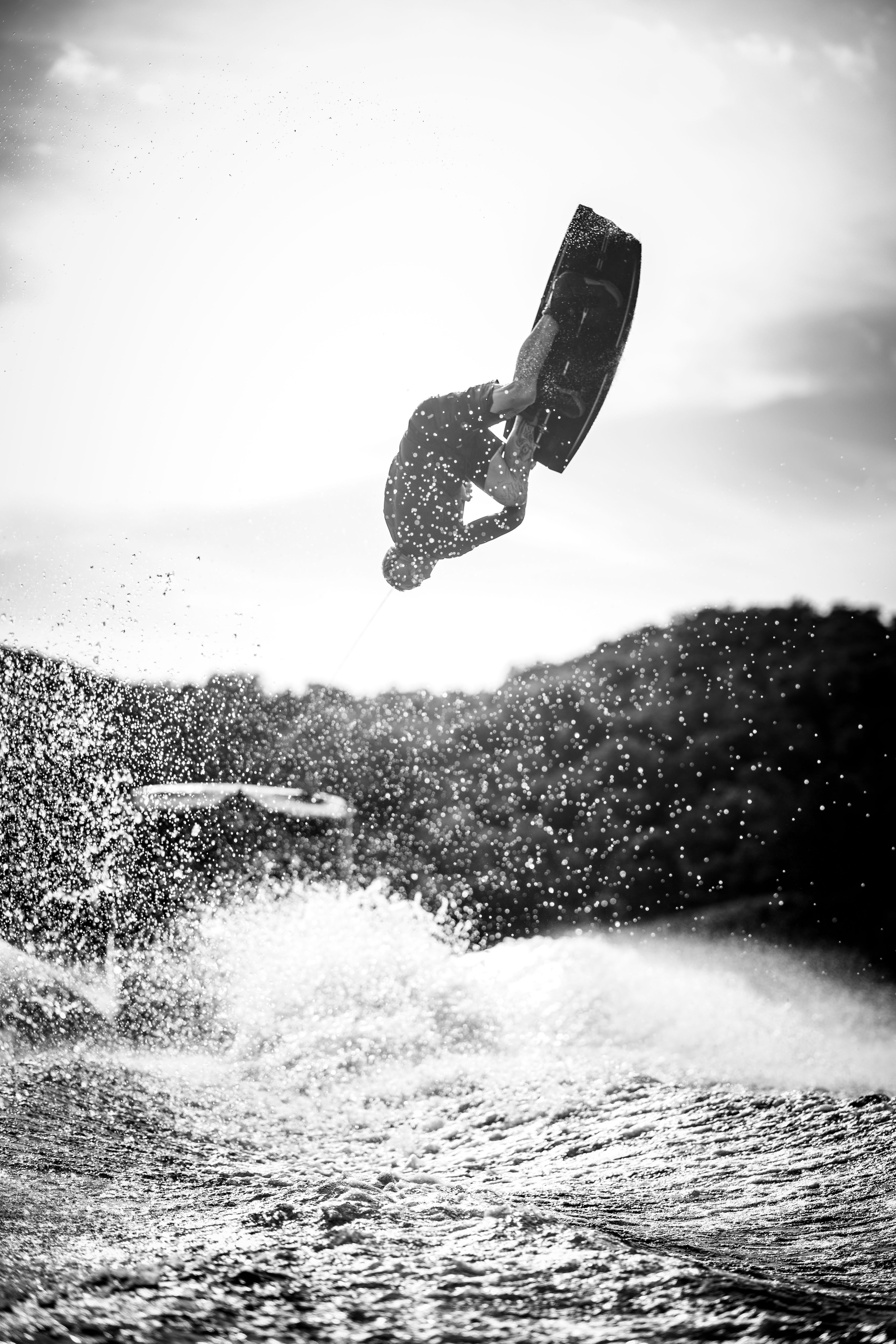 A person wakeboarding, performing an aerial flip above splashing water.