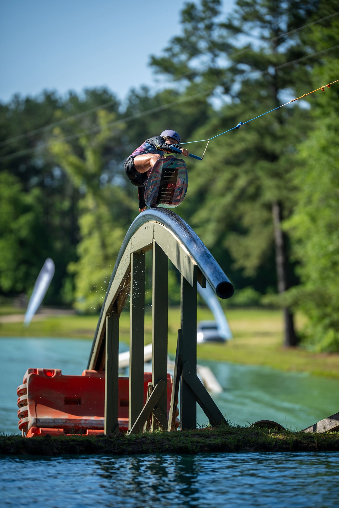 Wakeboarder performing a trick on a rail above water surrounded by trees.