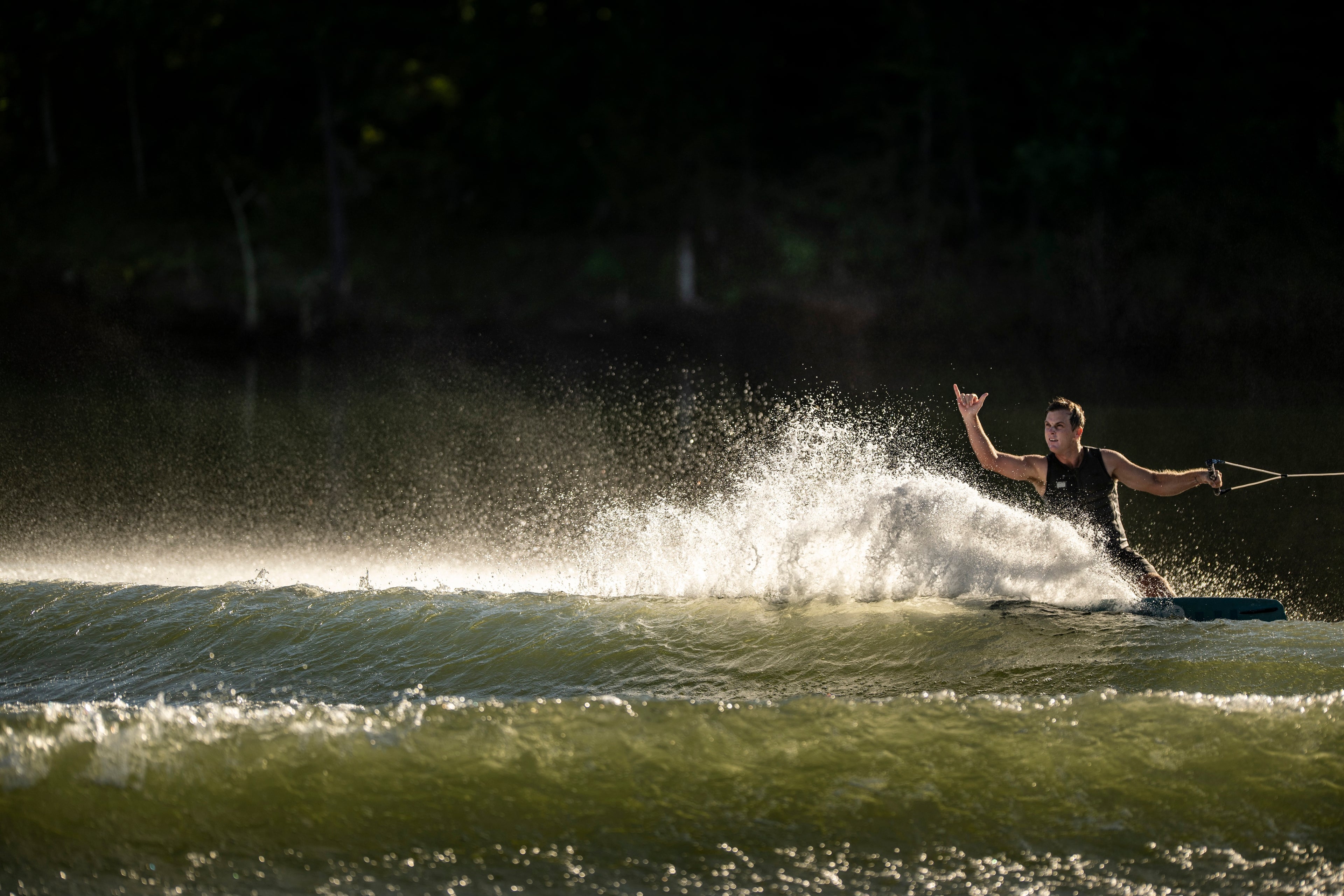 Person wakeboarding, creating a large spray of water, with a dark background.