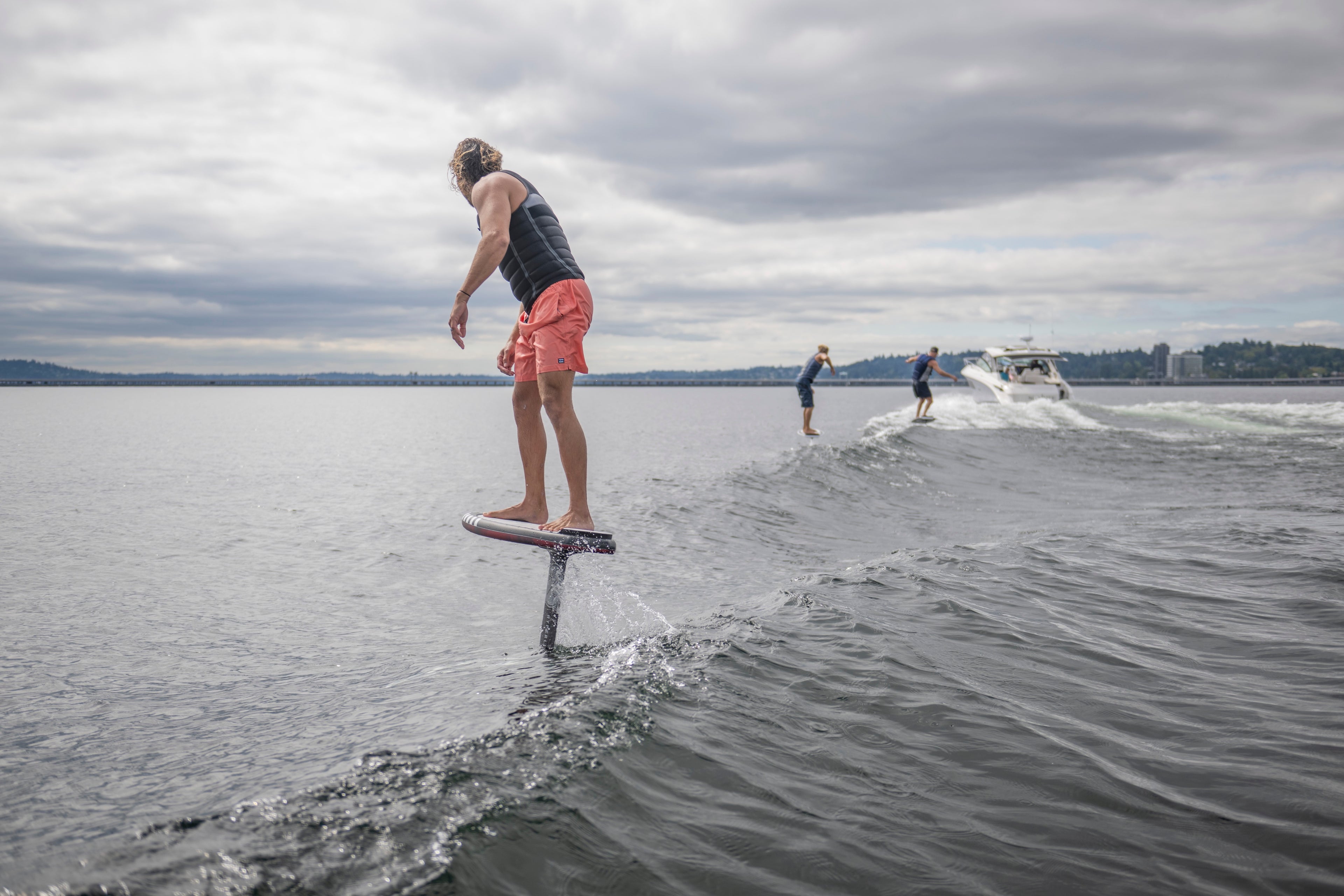 Man riding a hydrofoil on a lake, with a boat and two people in the background.