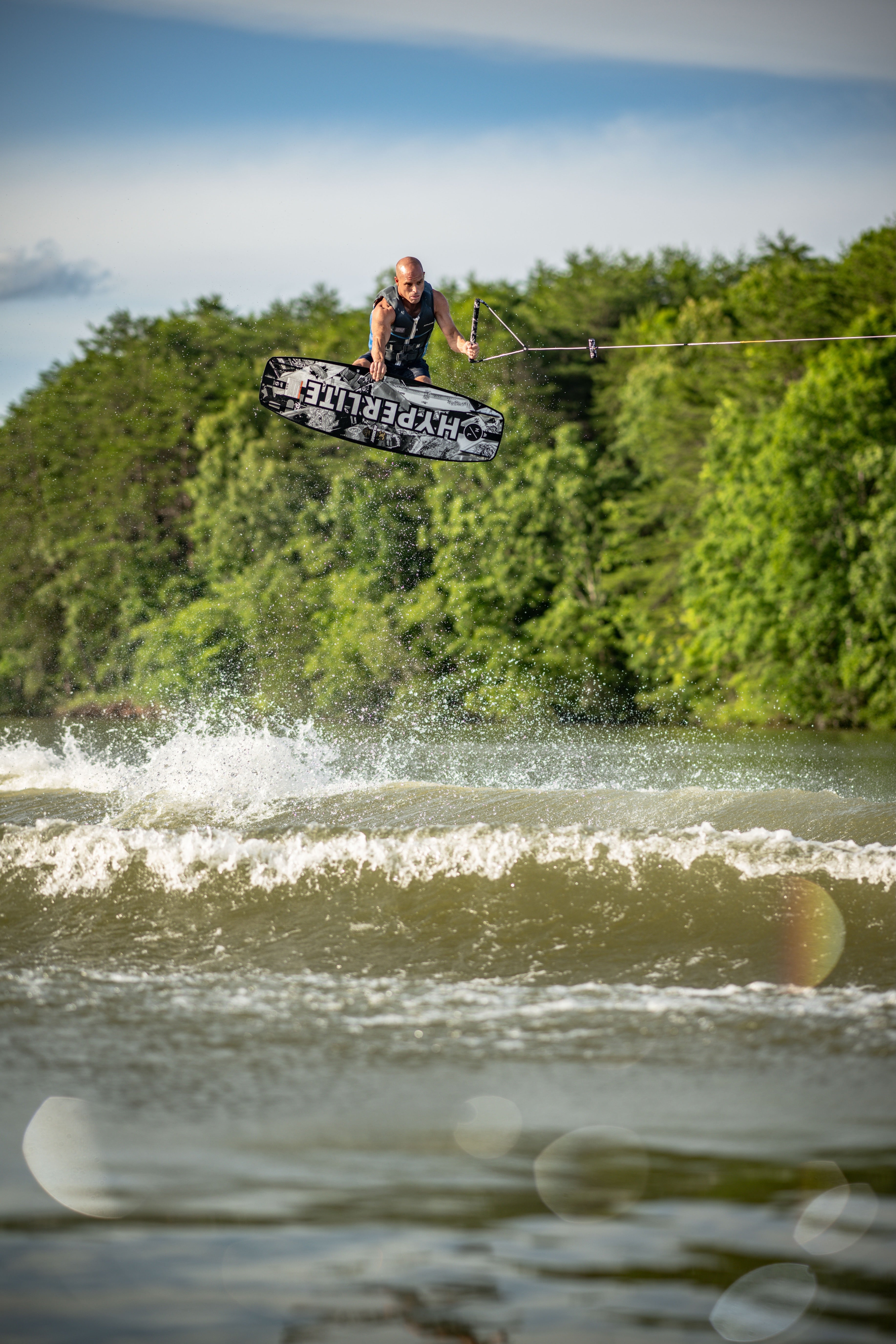 Person wakeboarding in the air, surrounded by trees and water splashes.