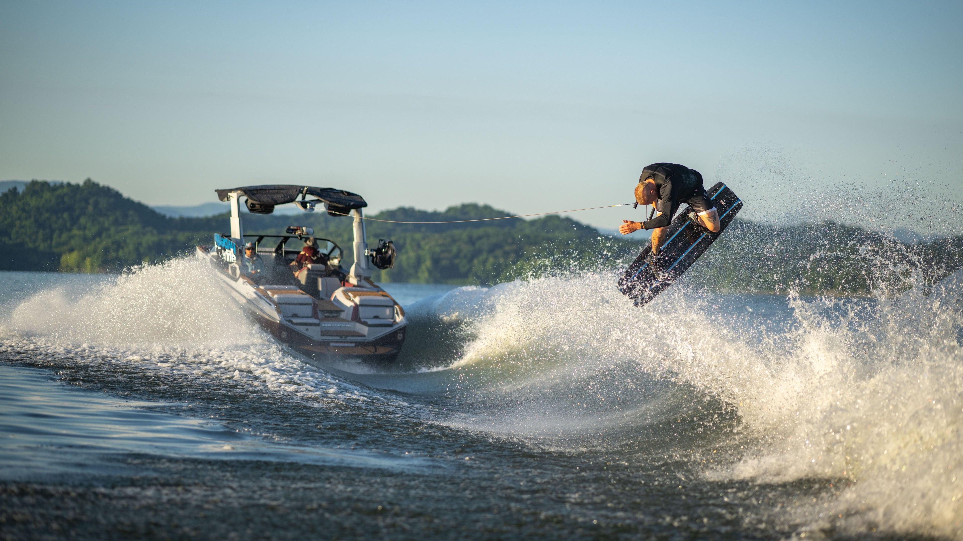 Person wakeboarding, performing a jump behind a boat on a sunny lake.