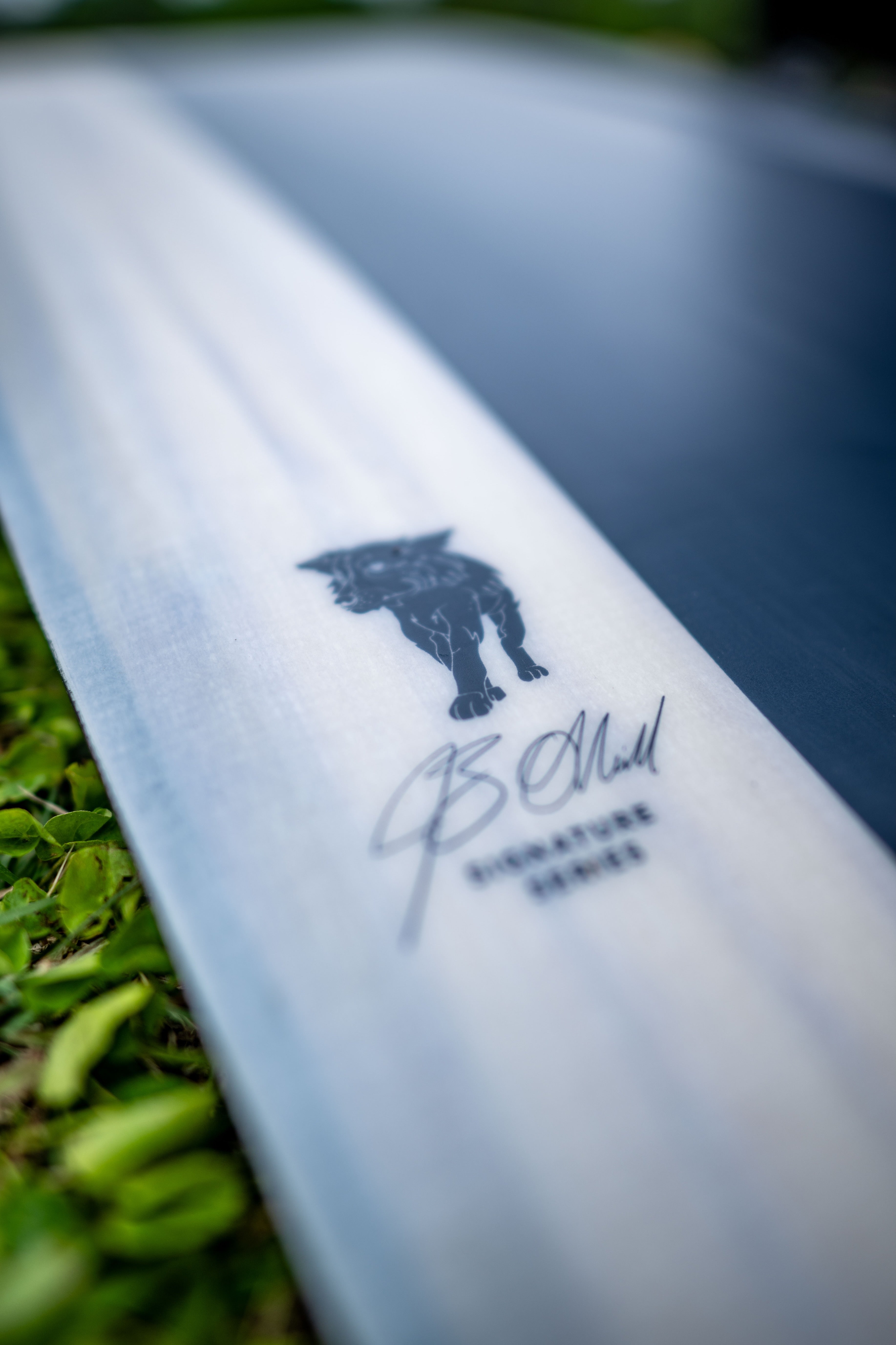 Close-up of a surfboard on grass, featuring a black panther logo and a signature.