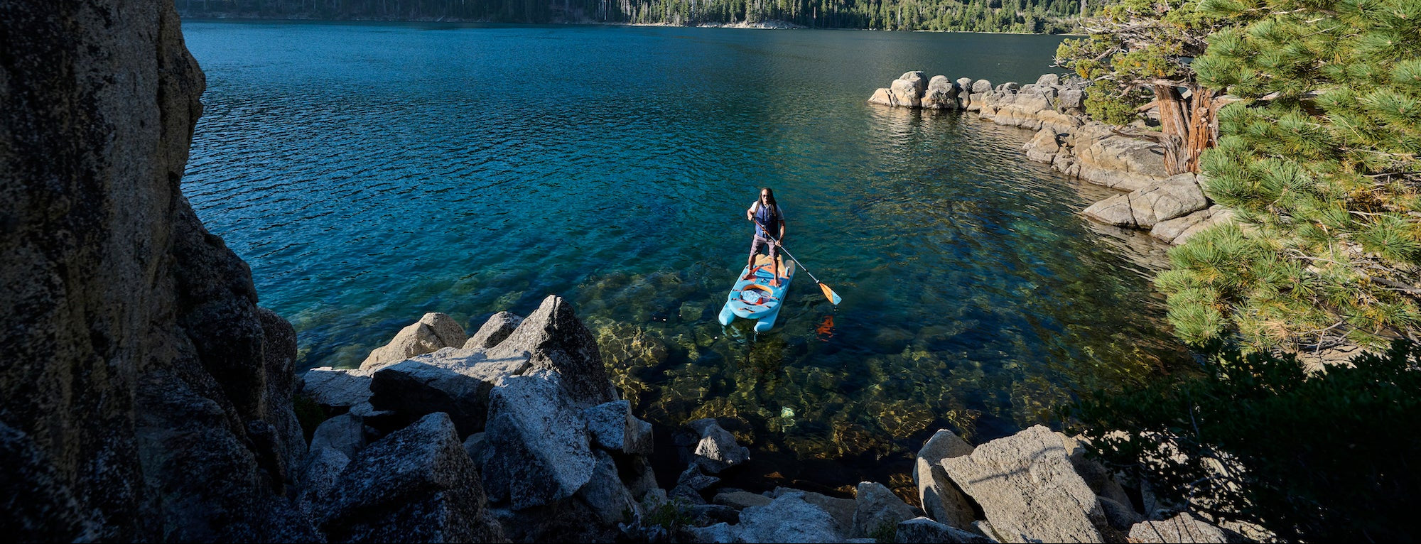 Person paddleboarding on a lake surrounded by rocky cliffs and trees.