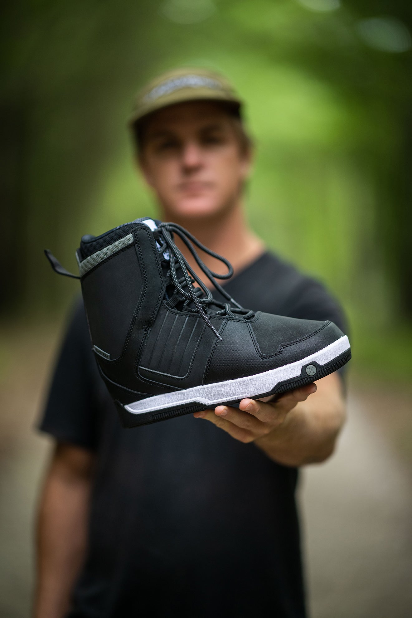 Person holding a black boot towards the camera in a blurred forest background.